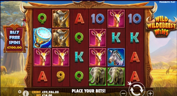 A Wild Wildebeest Wins slot game screen by Pragmatic Play shows a 5x4 reel grid with safari-themed symbols, a BUY FREE SPINS option for €700.00, a credit of €99,986.00, a bet of €14.00, and a PLACE YOUR BETS! message, set against a safari backdrop.